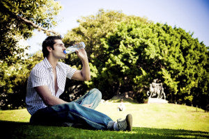Young man sitting in the park and drinking water from the bottle. - summer heat