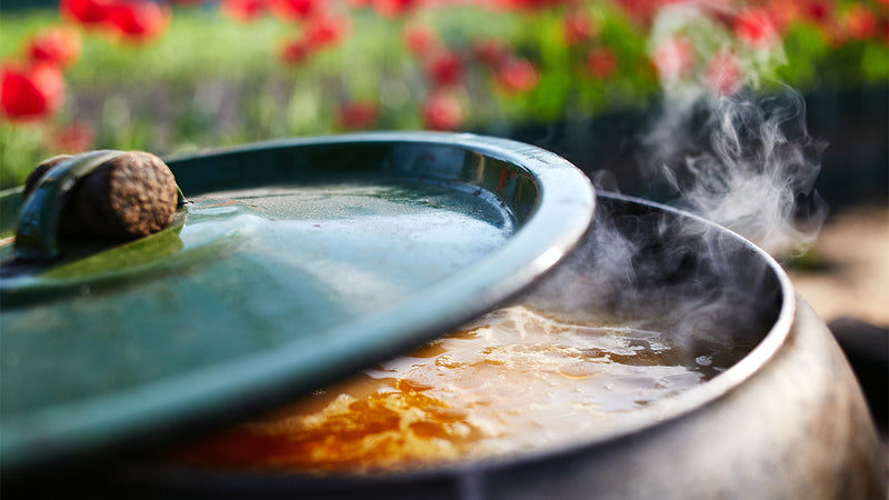 A large pot with a stew cooking inside on an outdoor stove.