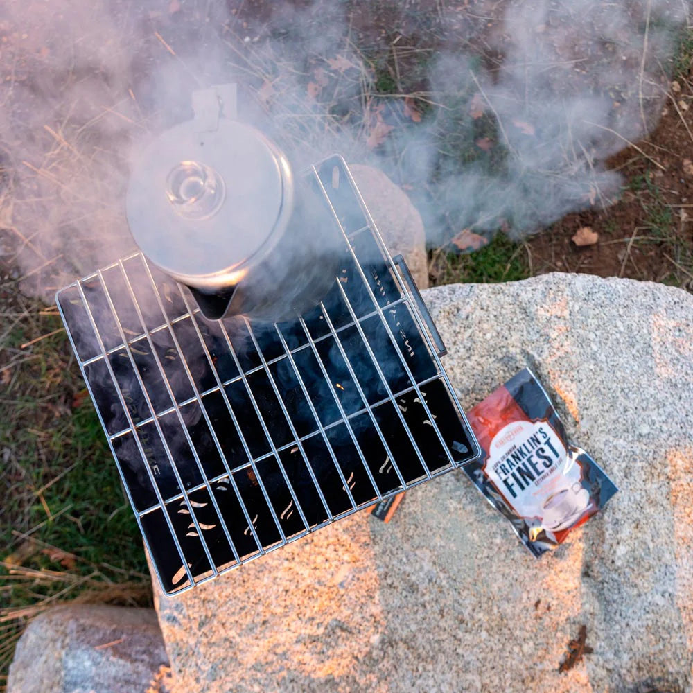 InstaFire Chimney Grill heating kettle next to Franklin's Finest coffee pouch in an outdoor setting