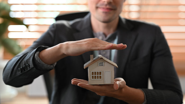 man holding his hand over a miniature house