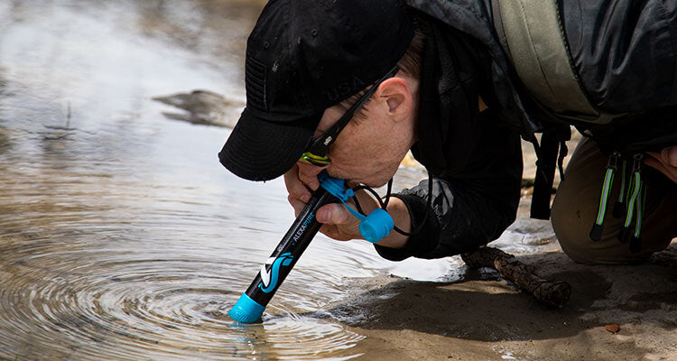 man drinking water from river using survival spring filter straw